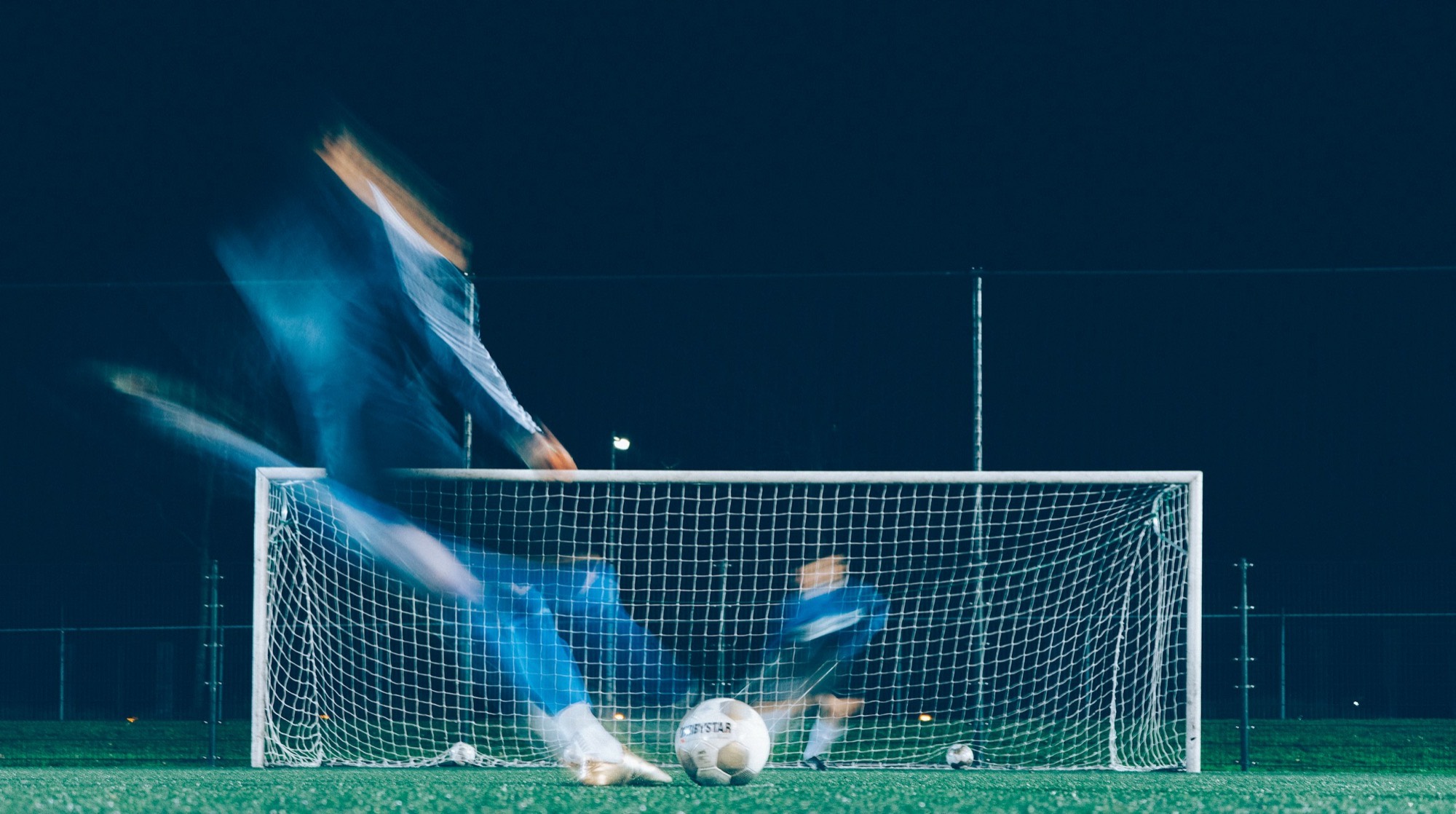 Long exposure of a player striking the ball in front of the goal under floodlights